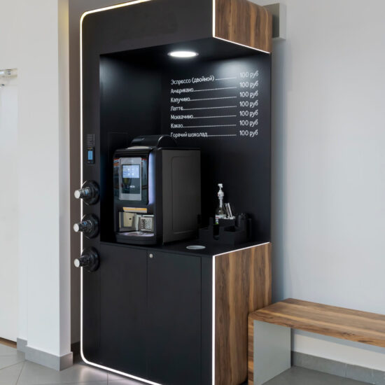 Russia, Moscow - November 21, 2021: Automated self-service cafe stands with bench by the wall of building. Table top vending coffee machine stands on black wooden furniture. Vending theme.